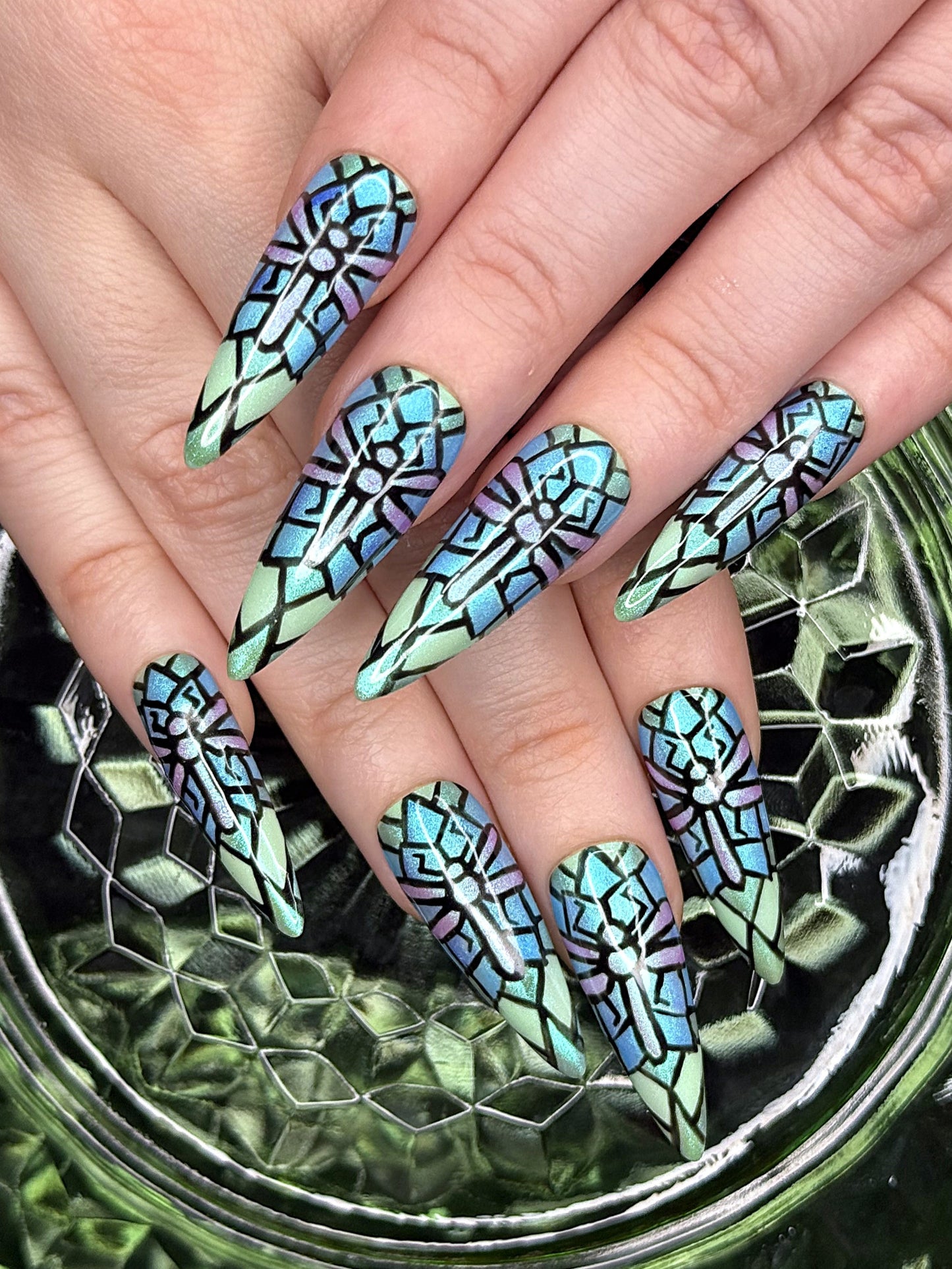 A picture of stained glass dragonfly press-ons on two hands. The background is green glass.