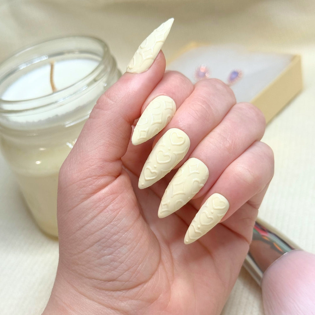 Powder Puff press-on nails on a left hand. In the background there is a candle, a box of jewelry, and a makeup brush.
