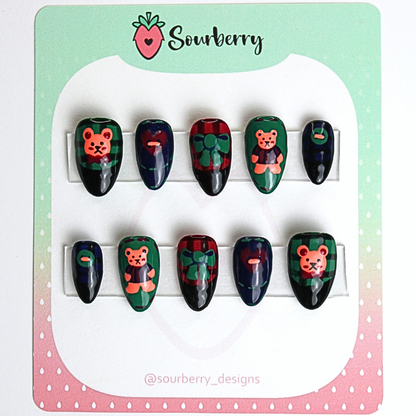 Patchwork Teddy press on nail set. The thumb nails and ring nails are green with a teddy bear painting. The index nails and pinky nails are dark blue with buttons. And the middle nails are red with green bows.