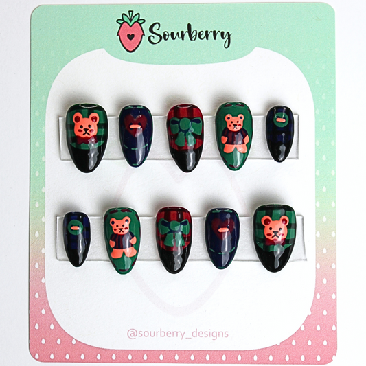 Patchwork Teddy press on nail set. The thumb nails and ring nails are green with a teddy bear painting. The index nails and pinky nails are dark blue with buttons. And the middle nails are red with green bows.