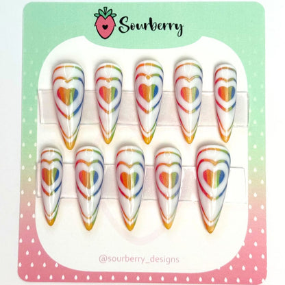 Rainbow Love Bomb nail set. This set has a white background with glittery rainbow heart patters on them. 