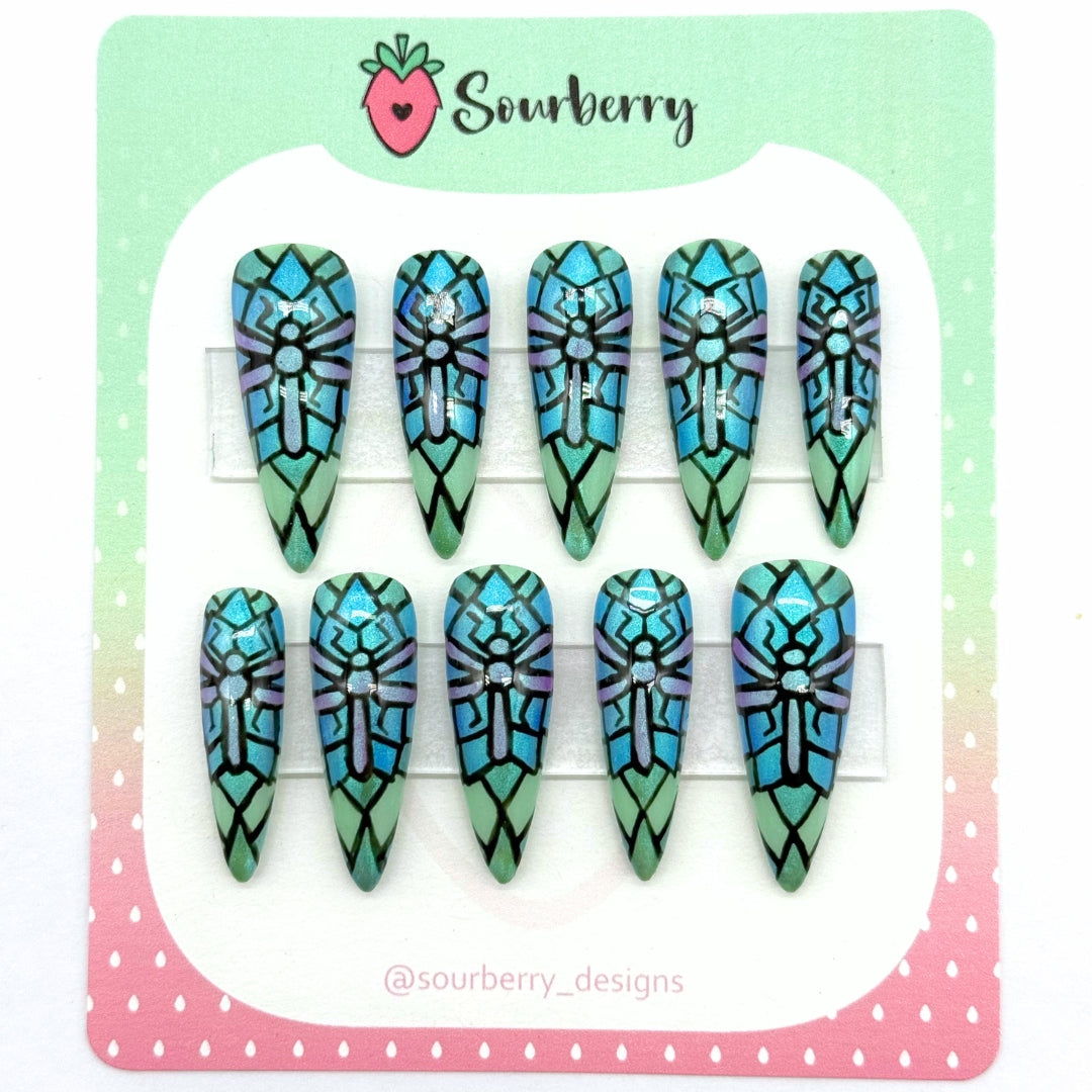 A picture of Sourberry brand "Stained Glass Dragonfly" press-on nails mounted on a green and pink card. The nails are sparkly with a stained glass pattern of a purple dragonfly on a blue and green background.